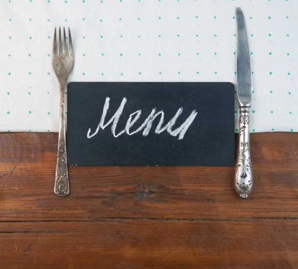 Menú escrito con tiza sobre pizarra envejecida con utinensil de cocina sobre mesa de madera. Vista superior - Foto, Imagen