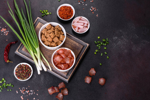 Dried meat slices with spices and herbs. Snacks for beer On a black stone background. Top view - Fotografie, Obrázek