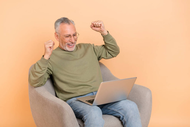 Photo of hooray old grey hairdo man sit look laptop wear eyewear pullover jeans isolated on beige background - Valokuva, kuva