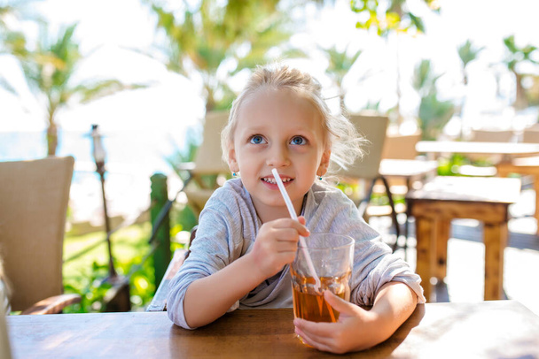 Adorable little girl drinking lemonade with raspberry and basil at table in cosy outdoor cafe. Happy and healthy childhood concept. Copy space - Fotografie, Obrázek