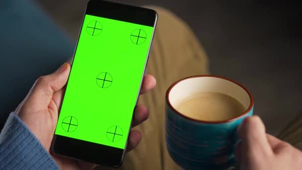 Человек, использующий смартфон с зеленым макетом экрана в вертикальном режиме и пить кофе. Человек просматривает Интернет, смотрит контент, видео. - Кадры, видео