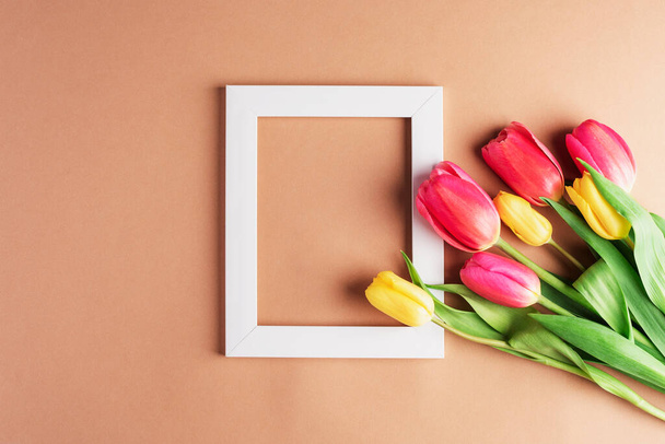 Cornice bianca con fiori di tulipano su sfondo neutro. Concetto vacanze primaverili. Vista dall'alto, posizione piatta, mockup. - Foto, immagini