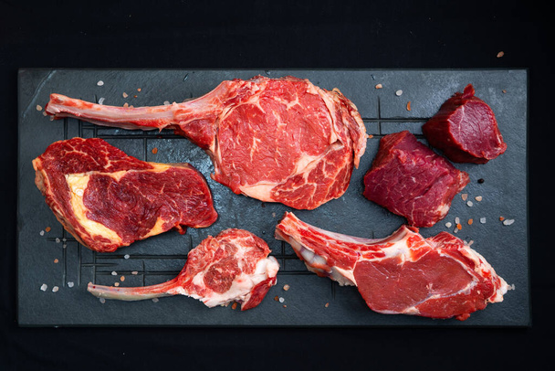 assorted raw beef steaks with salt on black background - Foto, afbeelding