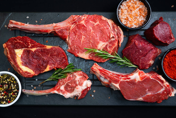 syrové hovězí steaky se solí, kořením a bylinkami na černém pozadí - Fotografie, Obrázek