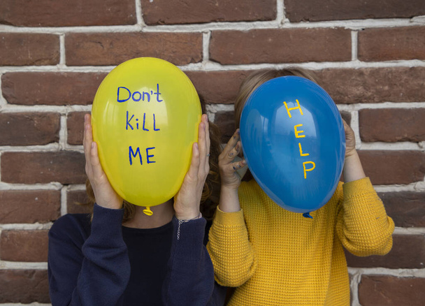 Twee onherkenbare mensen met blauwe gele ballonnen in plaats van gezicht met inscripties doden mij niet en helpen niet. Kinderen tegen oorlog. Angst, wanhoop, aandacht vestigen op militair conflict in Oekraïne - Foto, afbeelding