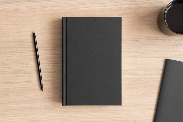 Zwart boek mockup met een kopje koffie en werkruimte accessoires op de houten tafel. - Foto, afbeelding