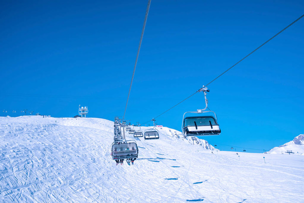 Ski lift moving over snowy landscape. Chairlift against clear blue sky. Tourists enjoying in winter. - Zdjęcie, obraz