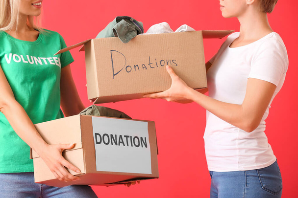 Young women holding boxes with clothes for donation on red background - Фото, изображение