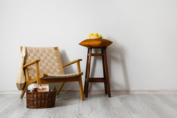 Comfortabele fauteuil, kruk en rieten mand bij lichte wand in het interieur van de kamer - Foto, afbeelding