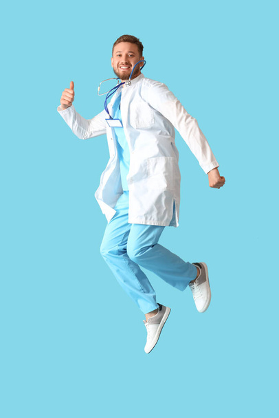 Young male doctor jumping on blue background - Photo, image