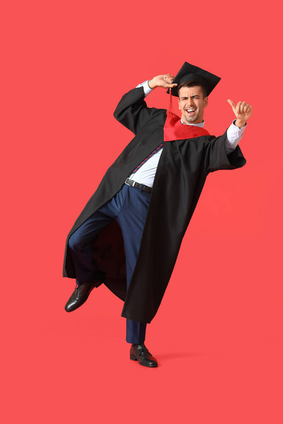 Young male graduate dancing on red background - Valokuva, kuva