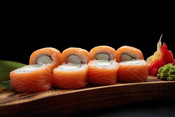 Sushi rolka Philadelphia, s wasabi a zázvorem, na dřevěné desce s listem bambusu, na tmavém pozadí - Fotografie, Obrázek