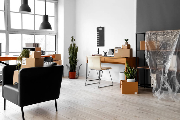 Cardboard boxes with belongings and furniture in interior of office on moving day - Fotó, kép
