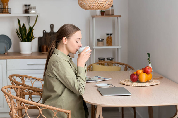 Junge Frau trinkt heißen Kaffee am Tisch in Küche - Foto, Bild