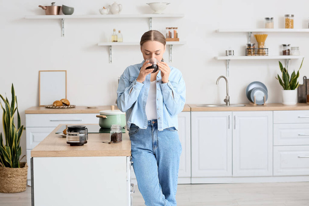 Young woman drinking tasty coffee in kitchen - 写真・画像