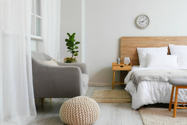 Cama confortável, mesa de cabeceira, poltrona e relógio no interior do quarto - Foto, Imagem