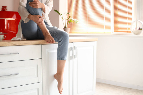 Barefoot woman sitting on counter in kitchen - Photo, Image