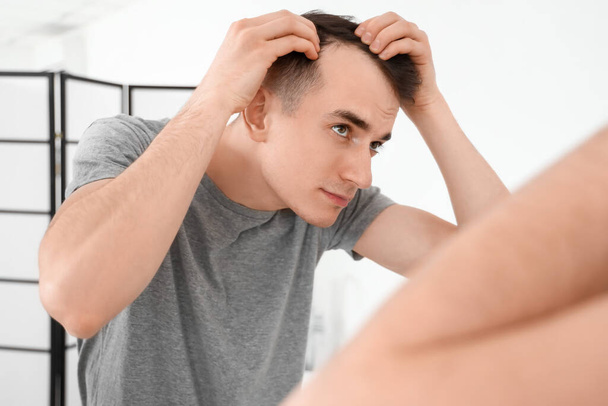 Молодой брюнет с проблемой выпадения волос у зеркала в ванной комнате - Фото, изображение
