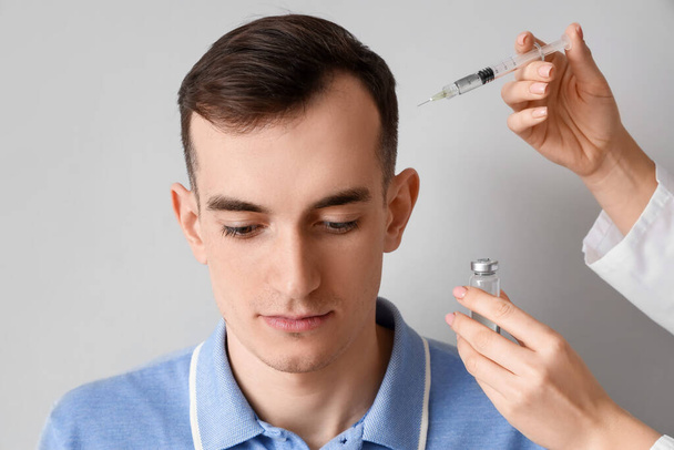 Hajhullási problémákkal küzdő fiatalember, könnyű háttérrel beadott injekció - Fotó, kép