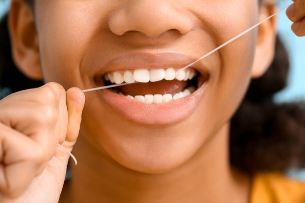 Afrikaans-Amerikaanse tiener meisje flossen tanden op blauwe achtergrond, close-up - Foto, afbeelding