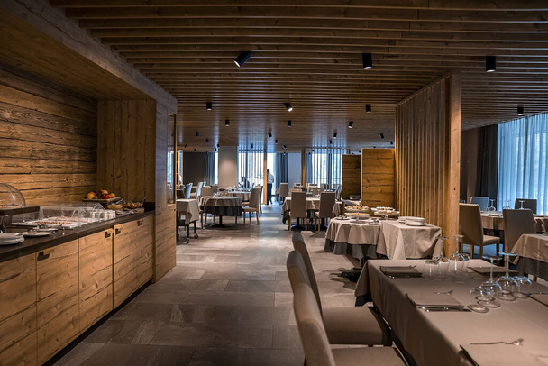 Tables and chairs arranged in spacious restaurant. Rustic style eating place at luxurious ski resort. Interior of dining hall in hotel - Foto, imagen
