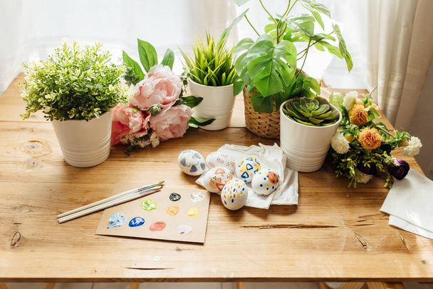 現代のイースターエッグが描かれています。花や植物でブラシや塗料。木製の背景に幸せなイースターの概念. - 写真・画像