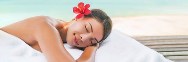 Massage spa and Body care outside on beach at luxury vacation resort. Asian beauty woman relaxing sleeping lying on table during aromatherapy treatment with coconut oil - Foto, afbeelding