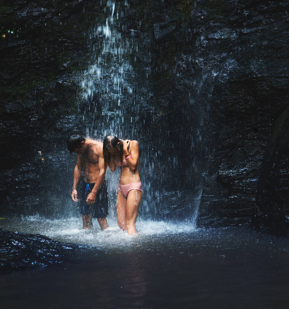 Lets stay like this for the whole day. Shot of two young people standing under a waterfall and enjoying every moment of it while looking down. - Photo, image