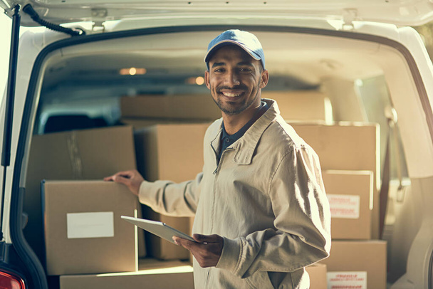 Mantener una entrega rápida y eficiente. Retrato de un repartidor usando una tableta digital mientras marca las cajas de su furgoneta. - Foto, imagen