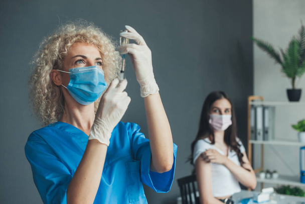 Кавказька жінка, одягнена в маску обличчя, отримує страшне ін'єкції вакцини, а лікар готує шприц для вакцинації в лікарні. Для медичного дизайну. Тримаючи руки - Фото, зображення