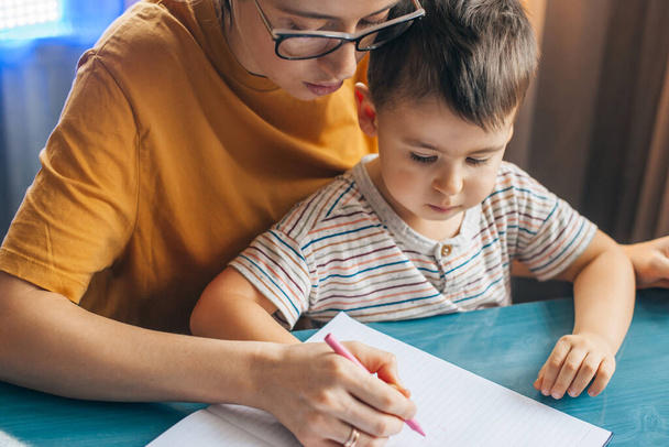 Улыбающаяся мать рисует картинку с маленьким сыном с карандашами. Счастливая семья. Закрыть. - Фото, изображение