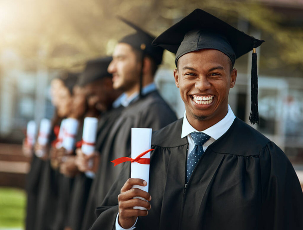 Imagine the doors this could open. Portrait of a young man holding his diploma while standing with his fellow students on graduation day. - Foto, imagen