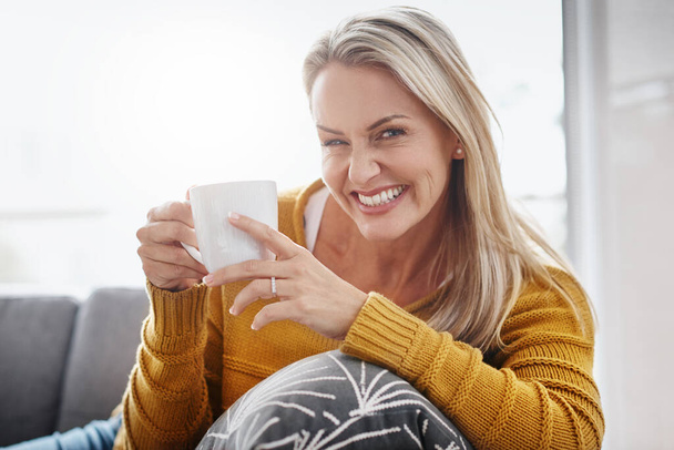 Для расслабления дома просто добавьте кофе. Портрет привлекательной зрелой женщины, наслаждающейся напитком, расслабляясь дома на диване. - Фото, изображение