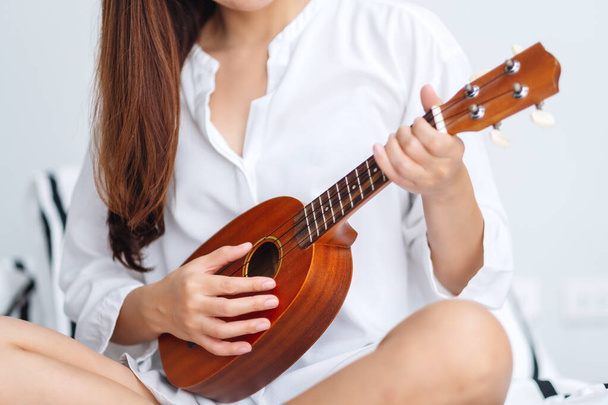 Крупный план женщины, сидящей и играющей на укулеле в спальне - Фото, изображение