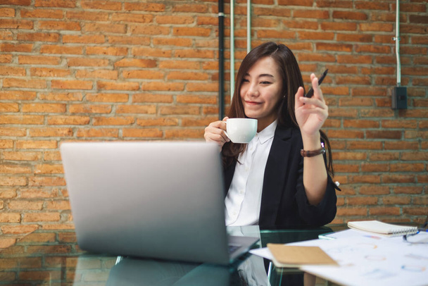 Nahaufnahme einer schönen asiatischen Geschäftsfrau, die Kaffee trinkt, während sie im Büro Laptop-Computer benutzt und arbeitet - Foto, Bild