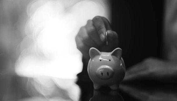 Black and white image of a woman putting coins into piggy bank for saving money concept - Photo, Image