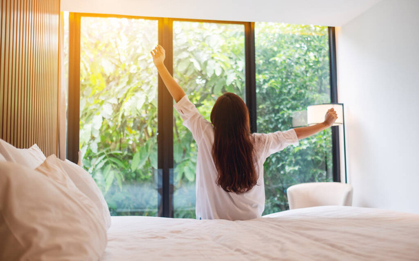 Rückseite Bild einer Frau tun Stretching nach dem Aufwachen am Morgen, Blick auf eine schöne Natur Blick außerhalb Schlafzimmerfenster  - Foto, Bild