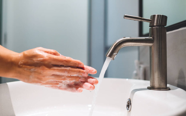 Mujer limpiando y lavando las manos con jabón debajo del grifo en el baño - Foto, imagen