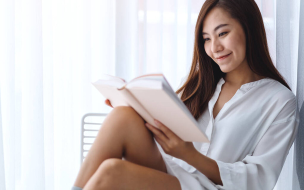 Close-up afbeelding van een mooie aziatische vrouw lezen boek in een slaapkamer thuis - Foto, afbeelding