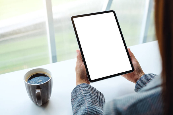 Mockup image of a woman holding black tablet pc with blank white screen with coffee cup on the table - Fotografie, Obrázek