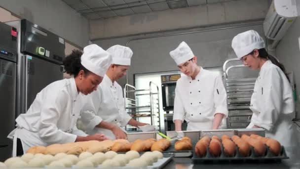 Multiraciale professionele gastronomische team, vier koks in witte kok uniformen en schorten kneden deeg en eieren, bereiden brood, en bakkerij voedsel, bakken in de oven in roestvrij stalen restaurant keuken. - Video