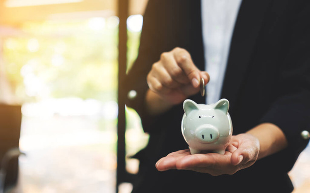 Closeup image of a businesswoman holding and putting coin into piggy bank for saving money and financial concept - Photo, Image