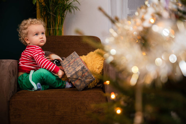 A child sits in a chair and looks at a decorated Christmas tree. - Foto, imagen
