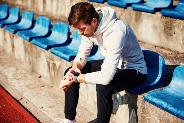 Uomo seduto al sedile dello stadio e controllare orologio fitness dopo gli esercizi - Foto, immagini