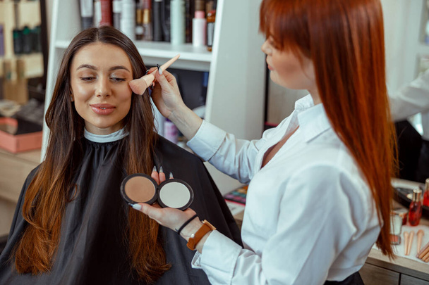 Professional makeup artist applying bronzer powder with a brush in beauty salon - Photo, Image