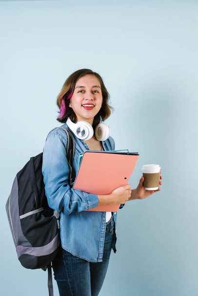 Jovem estudante hispânico mulher vestindo mochila e segurando livros e xícara de café sobre fundo azul isolado - Foto, Imagem