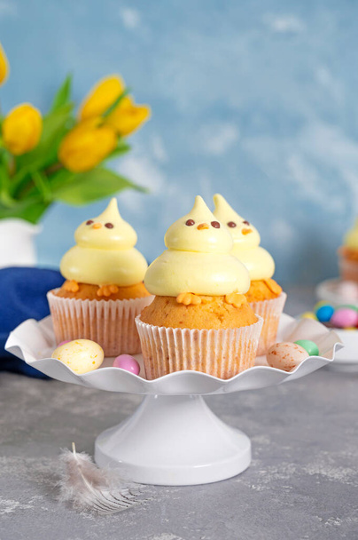 Cute Easter chick cupcakes. Vanilla cupcakes with buttercream on a white stand with fresh flowers on a white wooden background. Copy space - Photo, image