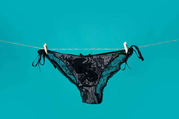 Black panties on rope. Sexy lingerie. Lace underwear. Womans black erotic panties. Womens panties hanging isolated on blue background. - Foto, immagini
