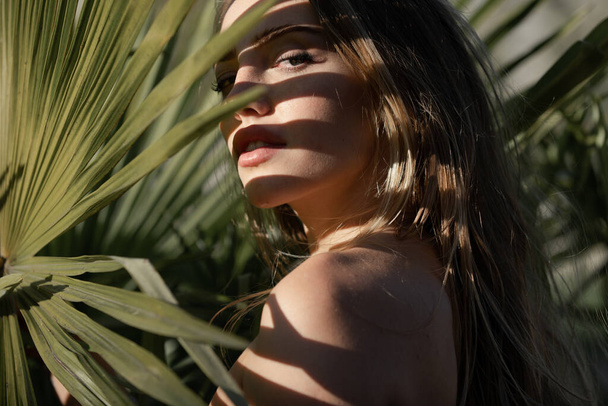 Portrait of beautiful woman with shadows of palm leaf on face. Young beautiful woman with shadow of palm leaves on face. Fashion shot of young gorgeous female. - 写真・画像