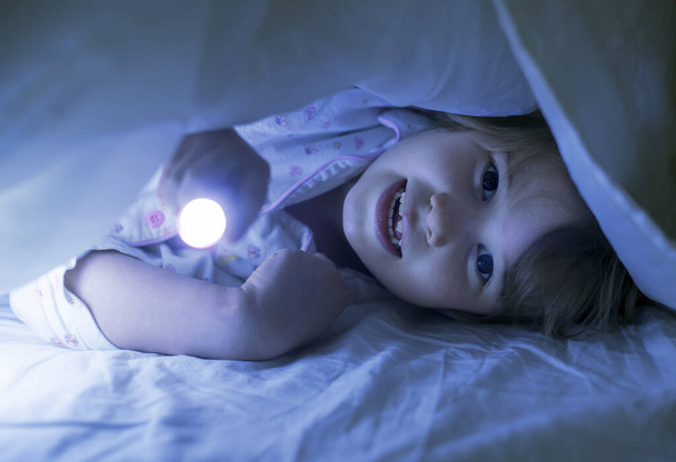 Młoda dziewczyna pod osłoną ze światłem w łóżku w nocy - Zdjęcie, obraz